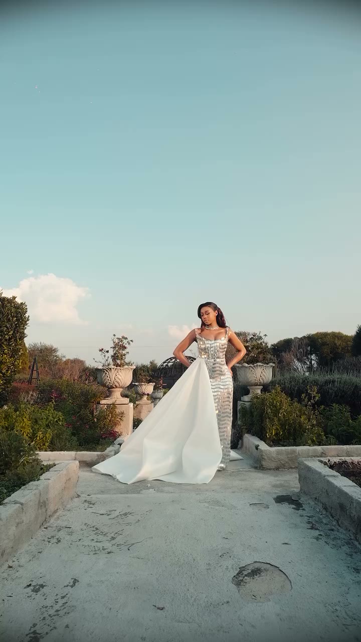 Bride on a garden terrace in a mirror-sequin column gown with a white satin overskirt trailing behind her